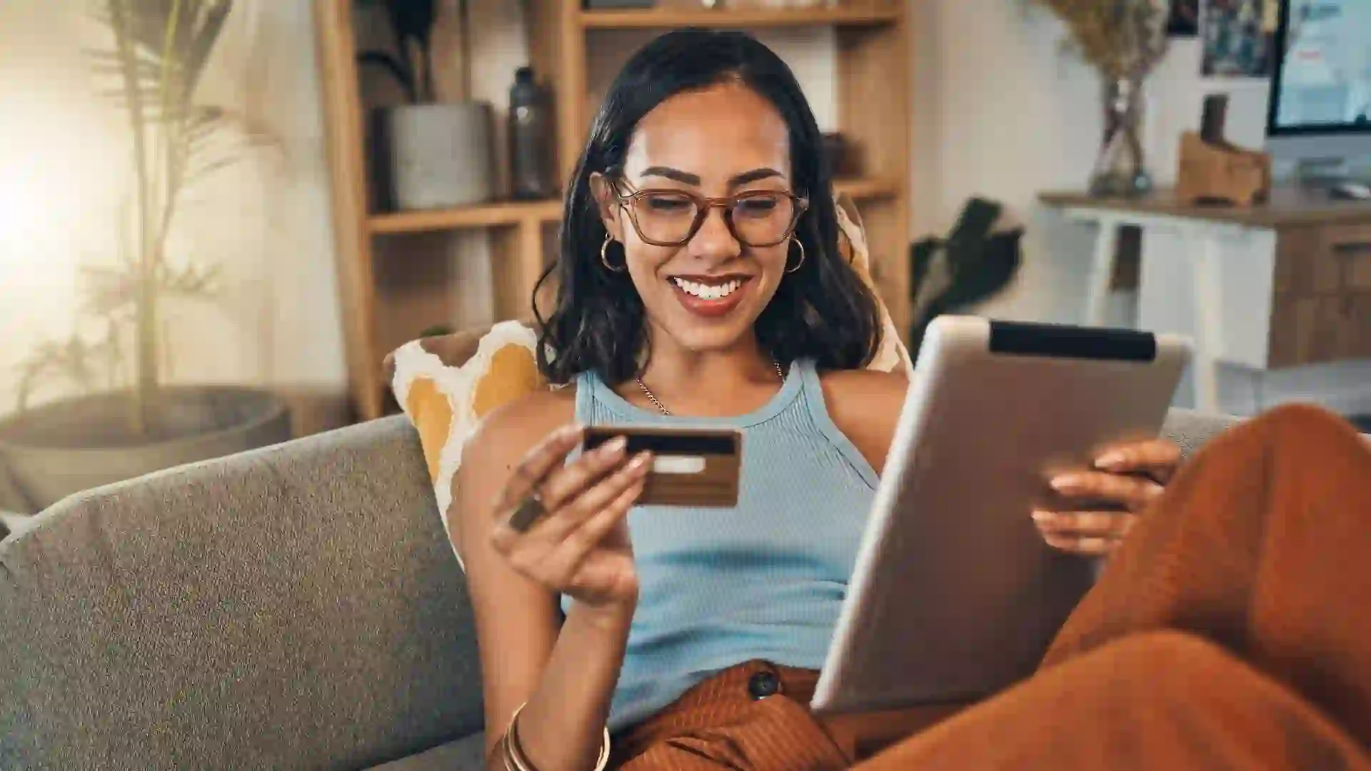 A woman smiles while holding her credit card and shopping online while holding her laptop.