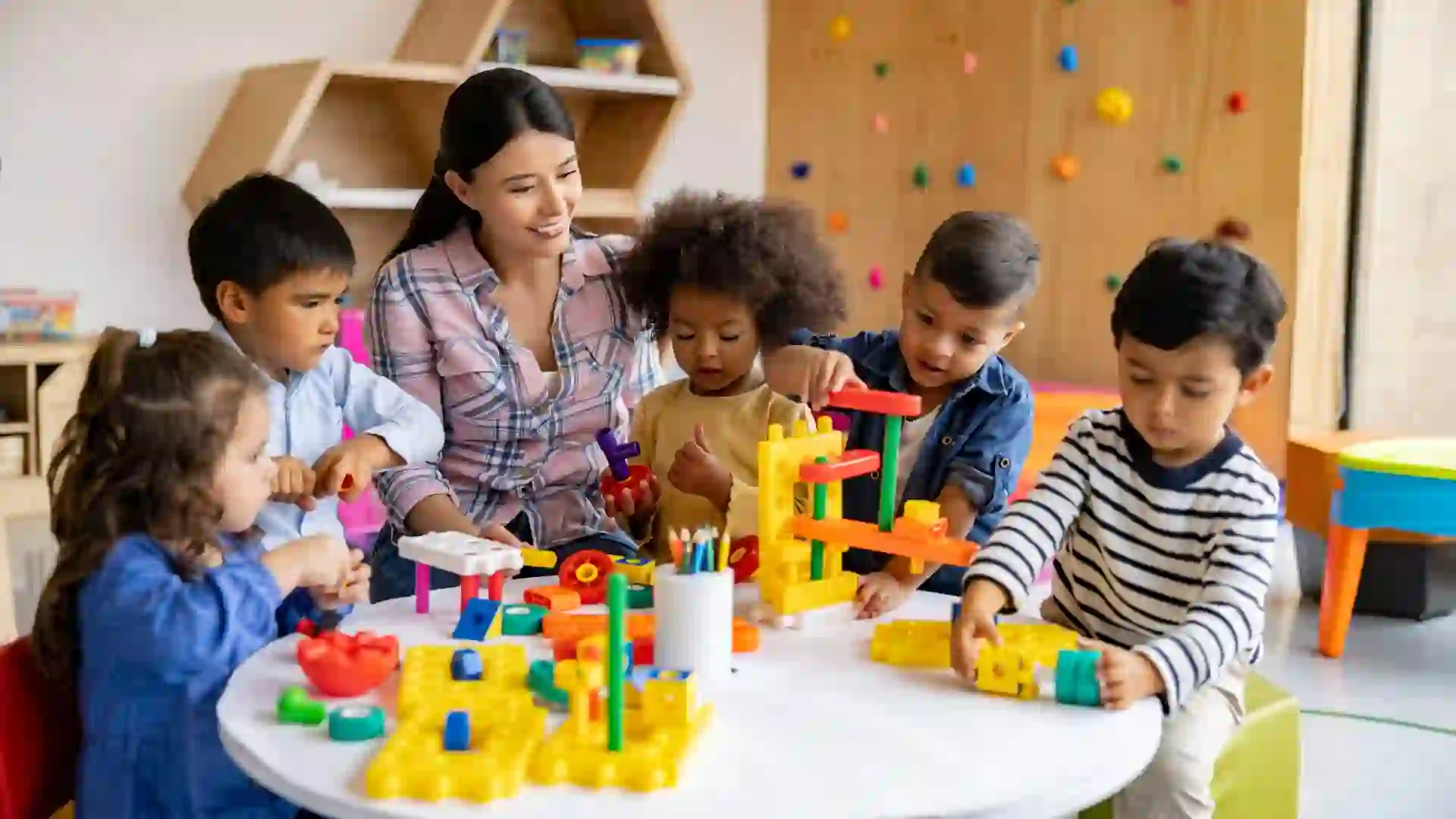 Happy Latin American teacher with a group of elementary students playing with toy blocks.