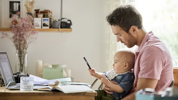 Father looking at baby boy playing with pen.