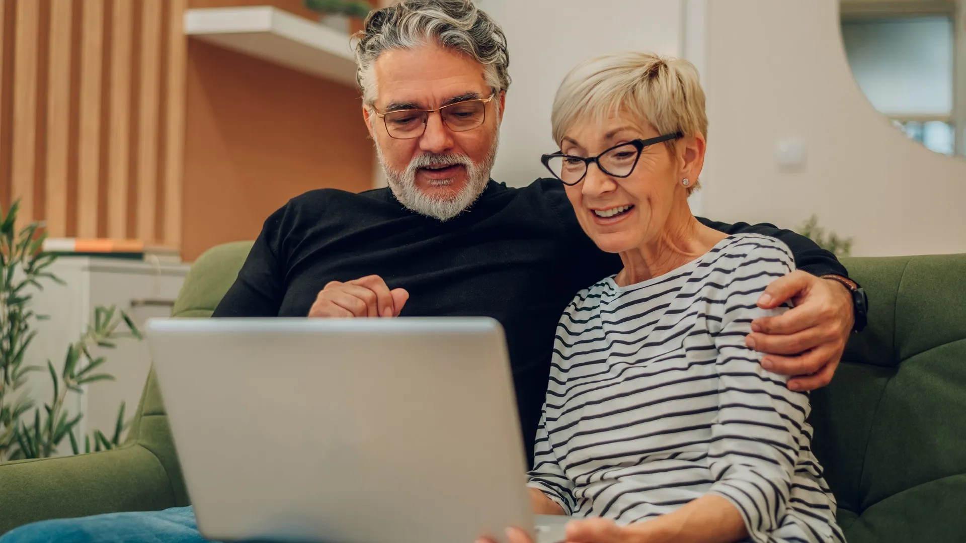 Senior couple using laptop while sitting on a couch at home stock photo