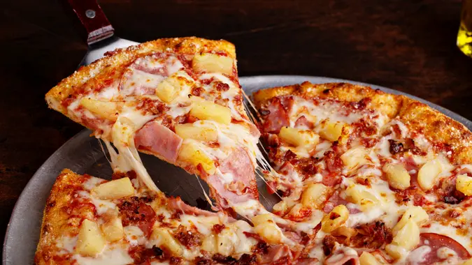 Hawaiian pizza with ham and pineapple cut into slices, cheese pull.