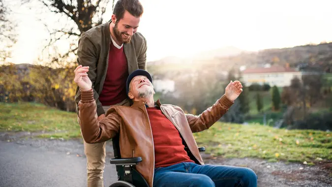 Young man and his senior father in wheelchair on a walk in town. stock photo