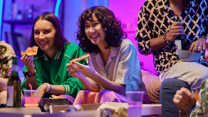 Two cheerful adolescent girls eating pizza and watching comedy on tv stock photo