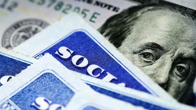 Several Social Security Cards on a US United States one hundred dollar bill $100 system of benefits for retired elderly people.