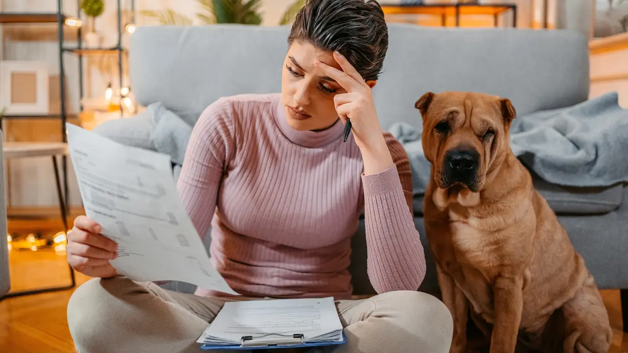 Woman checking her finances at home with her dog beside her, surrounded by bills and documents.