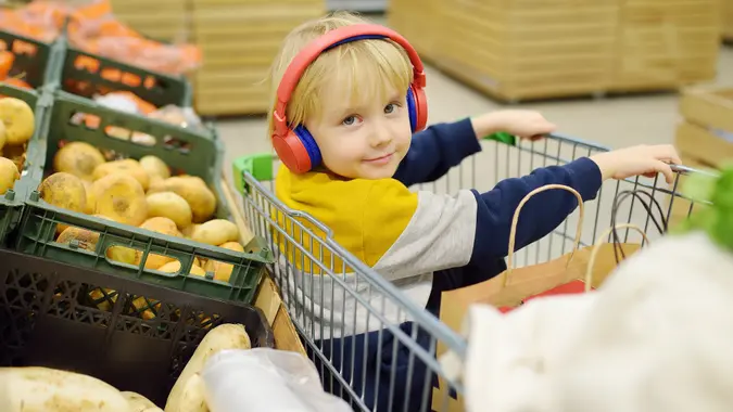 Cute preschooler boy with headphone and player is sitting in a shopping cart at a food store or supermarket. A child is listening to music or an audiobook while his parents buying groceries. stock photo