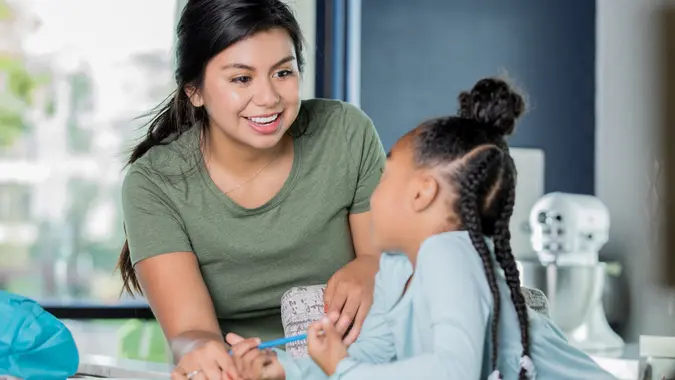 Happy young Hispanic woman is babysitting, tutoring elementary age girl. stock photo