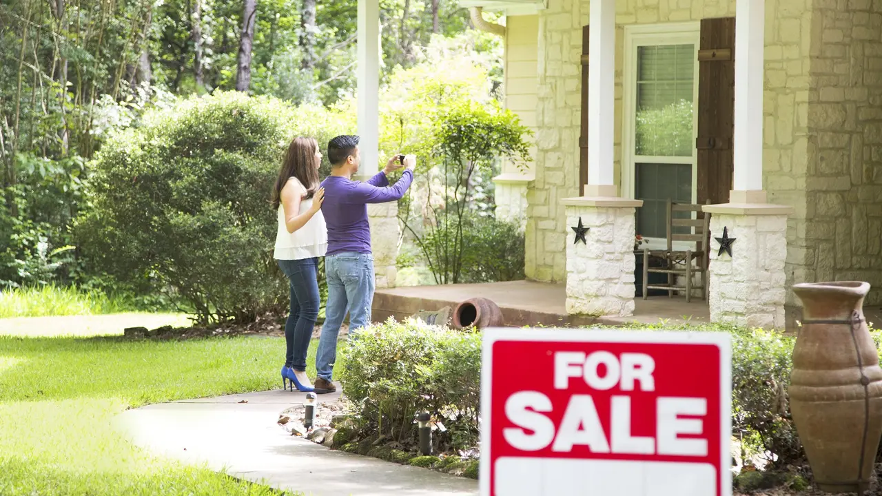 Mid adult couple are considering purchasing a new home. For sale sign in foreground. stock photo