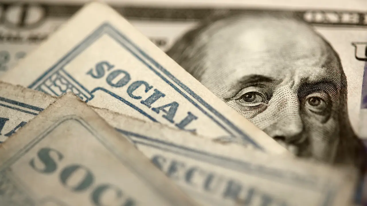 Several Social Security cards rest on top of a $100 bill.