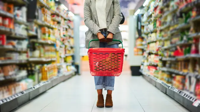 Supermarket aisle, woman legs and basket for shopping in grocery store.