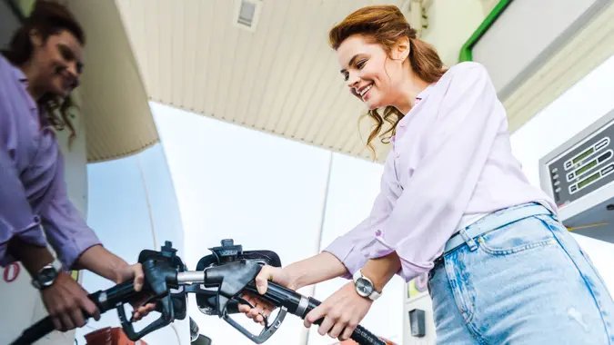 Low angle view of happy woman holding fuel pump while refueling car with benzine stock photo