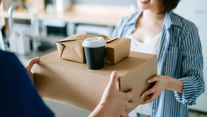 Close up of beautiful and cheerful young Asian woman receiving home delivery takeaway food order from a delivery man at home. Eating at home concept stock photo