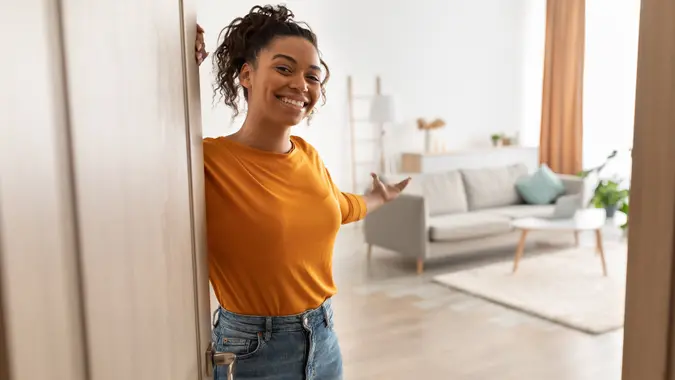 Cheerful African Woman Opening Door Welcoming You Standing At Home stock photo