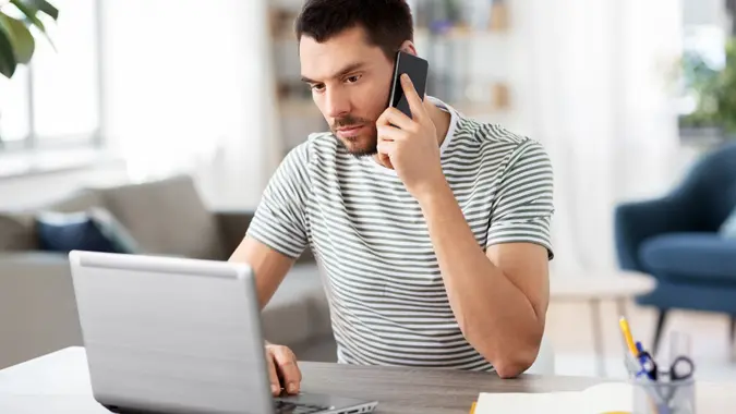 Man with laptop calling on phone at home office stock photo