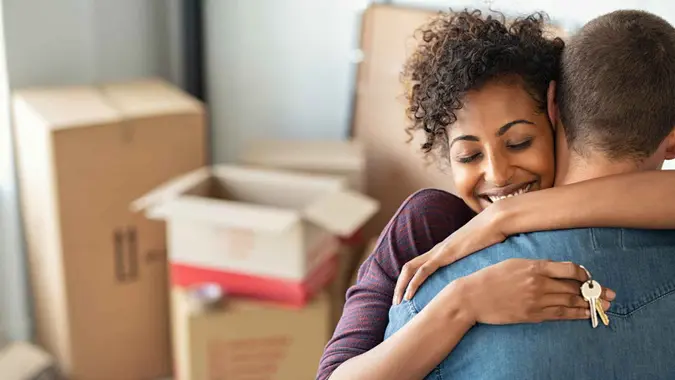 Young african woman holding home keys while hugging boyfriend in their new apartment after buying real estate.