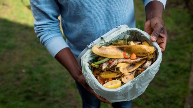 An aerial view of an unrecognizable person holding their plastic composting bin with items which are to go into their allotment in their larger composter ready to make into the soil for the following spring.