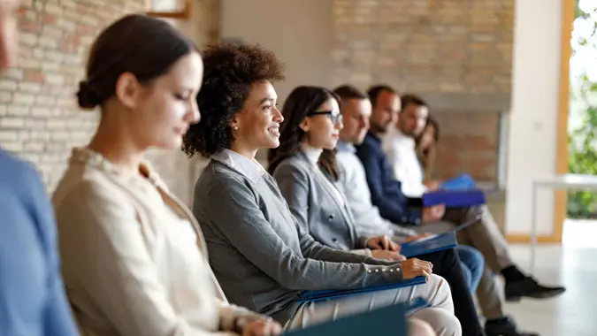 Large group of people sitting in waiting room before job interview for their potential business position.