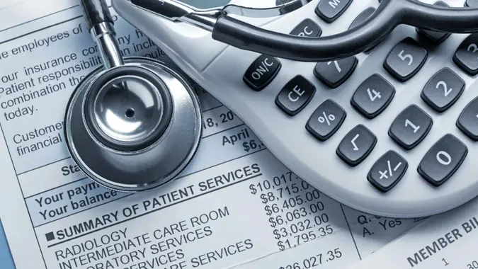 A stethoscope and a calculator rest on top of a medical bill.