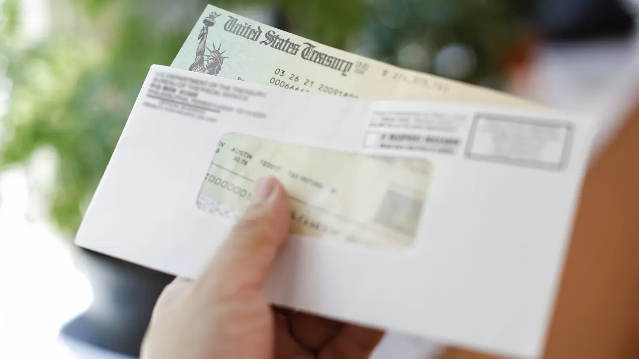 A man's hand holding an envelope and check from the U.S. Treasury.