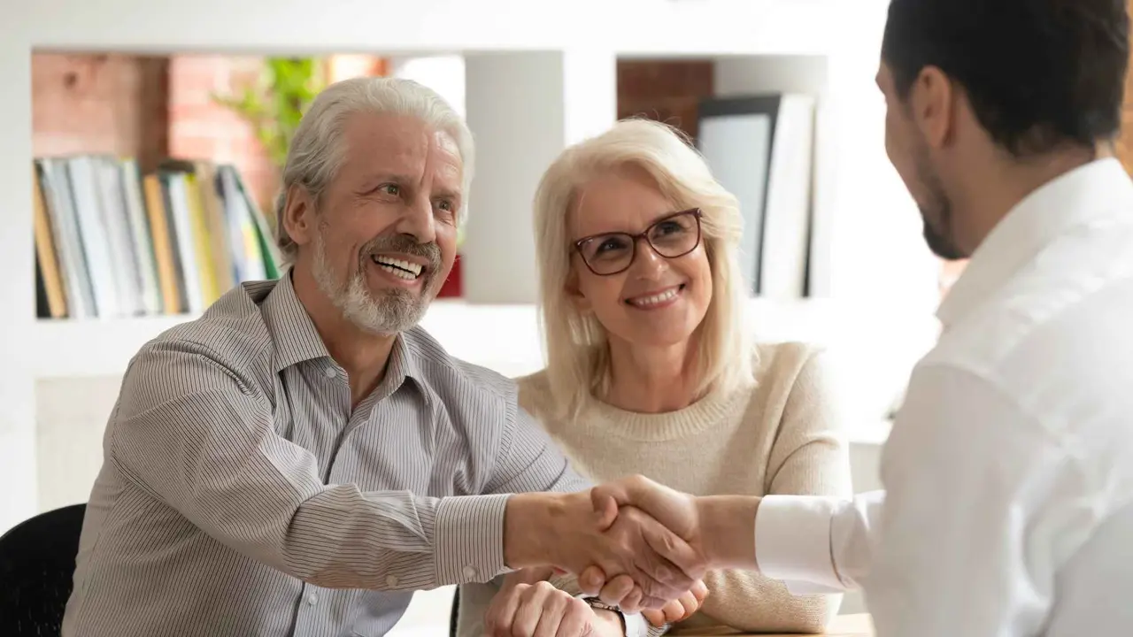 Happy senior old family couple clients make financial insurance estate business deal handshake agent lawyer, satisfied mature customers shake hand meeting bank manager agree on investment contract.
