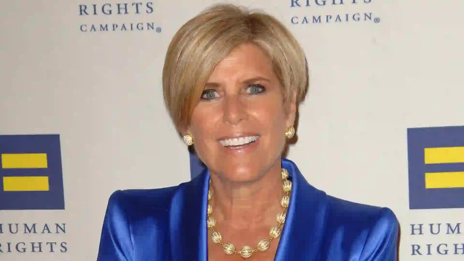 Suze Orman smiles while wearing a blue jacket