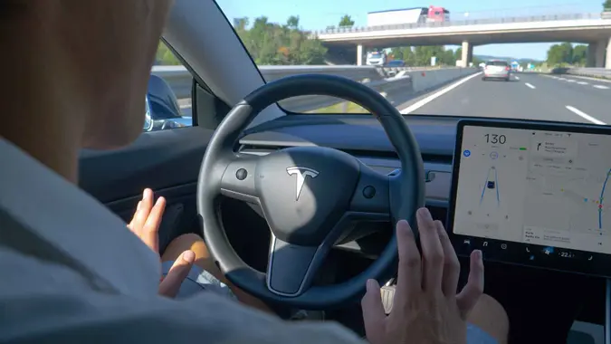 TESLA CAR, SLOVENIA, APRIL 2020: CLOSE UP: Unrecognizable man tentatively lets go of steering wheel of a Tesla after setting autonomous vehicle on auto-pilot.