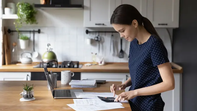 A woman calculates her expenses while standing in the kitchen