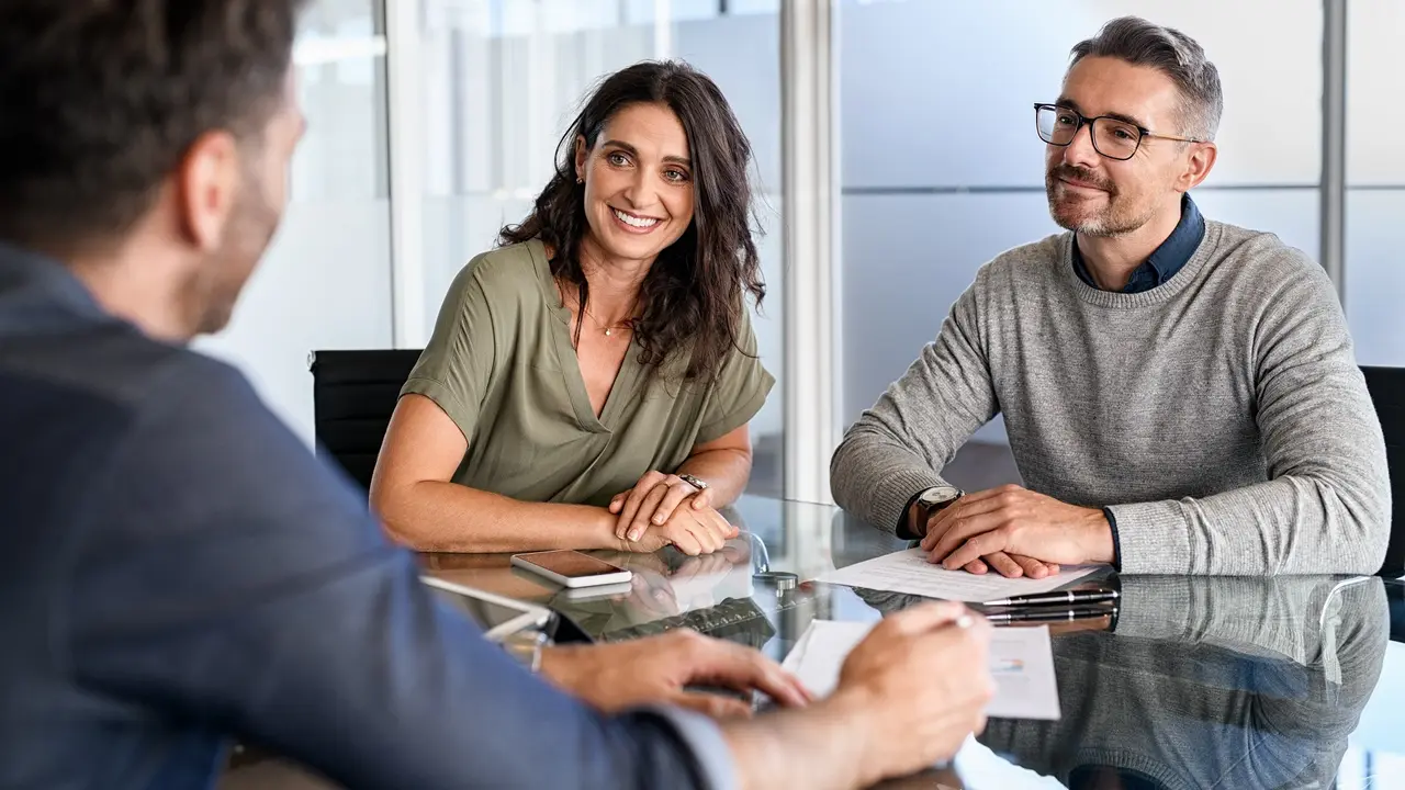 A couple meeting with and sitting at a table with a financial advisor at his office.