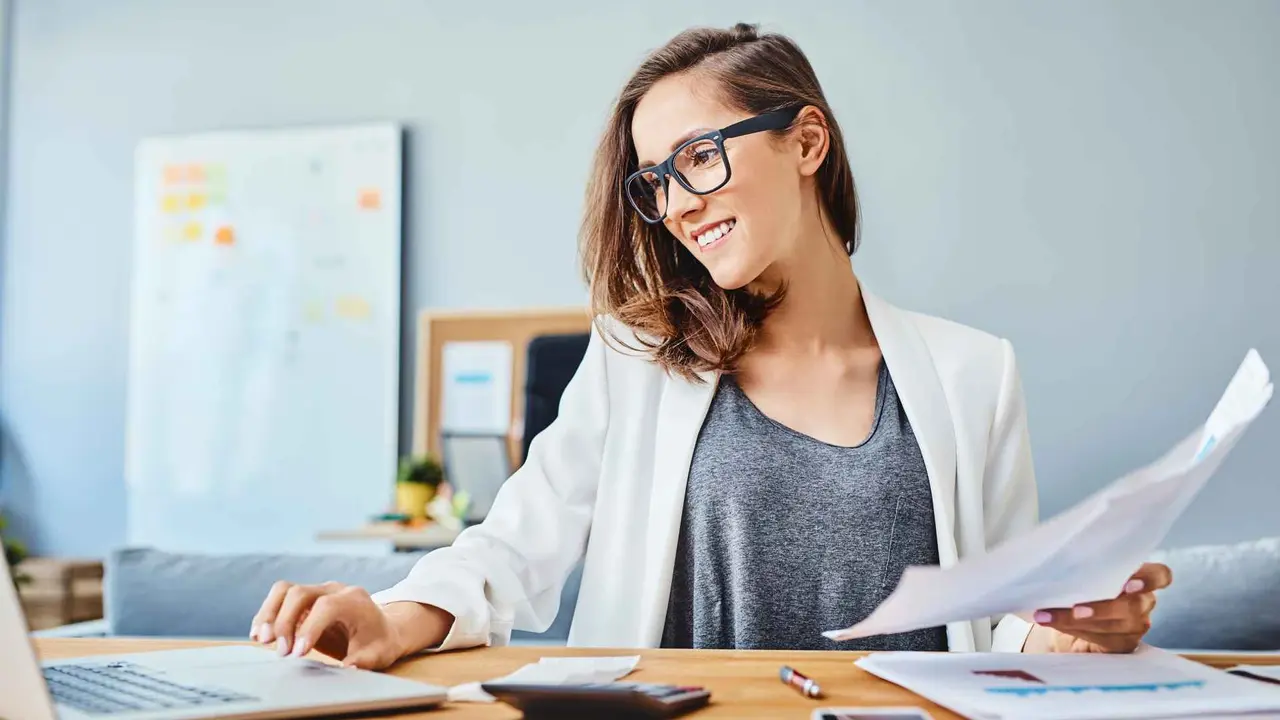 Cheerful young woman working with laptop and documents.