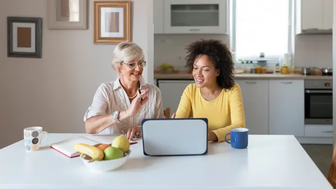 Mixed Race Adult Daughter Teaching Elderly Mother to Use Laptop at Home.
