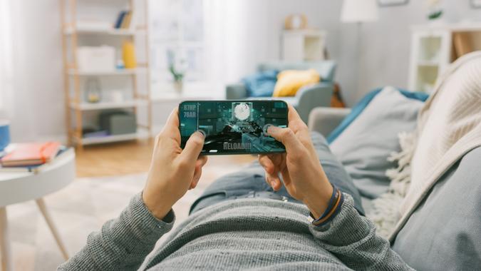 Man at Home Lying on a Couch using Smartphone, Holds it Horizontally in Landscape Mode.