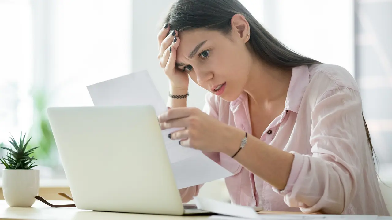 A young woman sitting at a table looks stress about her finances as she looks at a document.