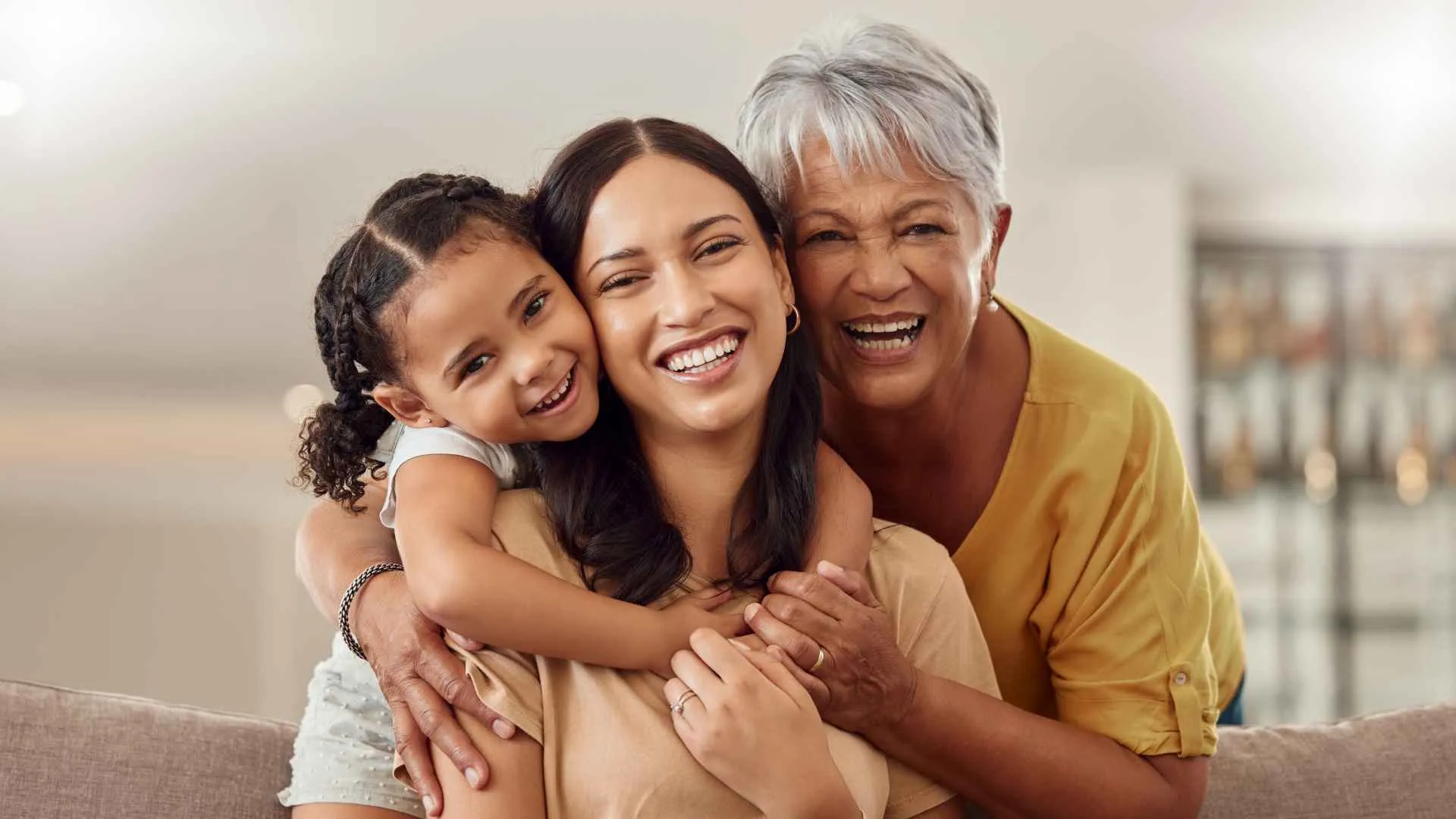 Grandmother, mom and child hug in a portrait for mothers day on a house sofa as a happy family in Colombia.
