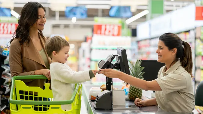 Cute little boy handing a loyalty card to cash register before scanning products at checkout in a supermarket stock photo