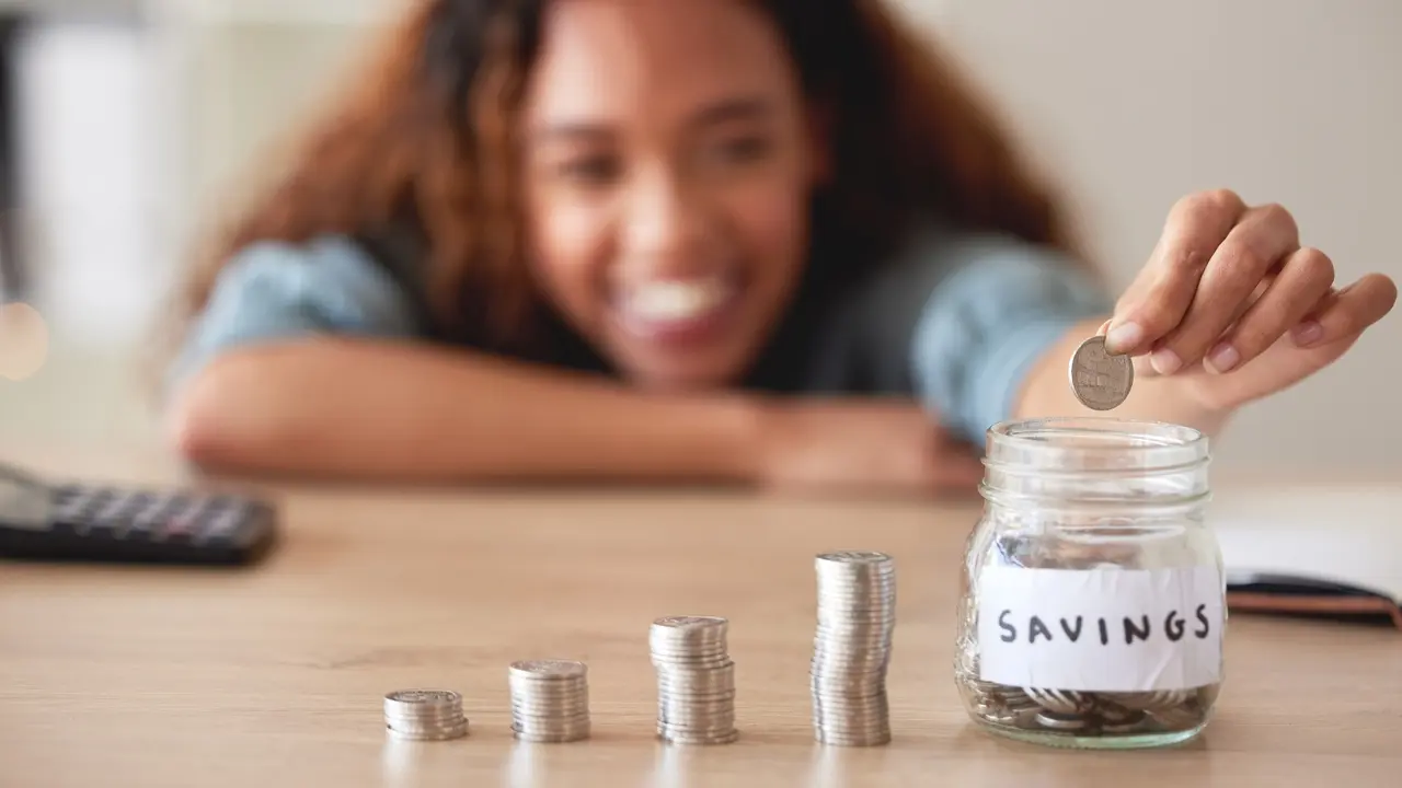 Unknown mixed race woman stacking a variety of coins and depositing them into a savings jar.