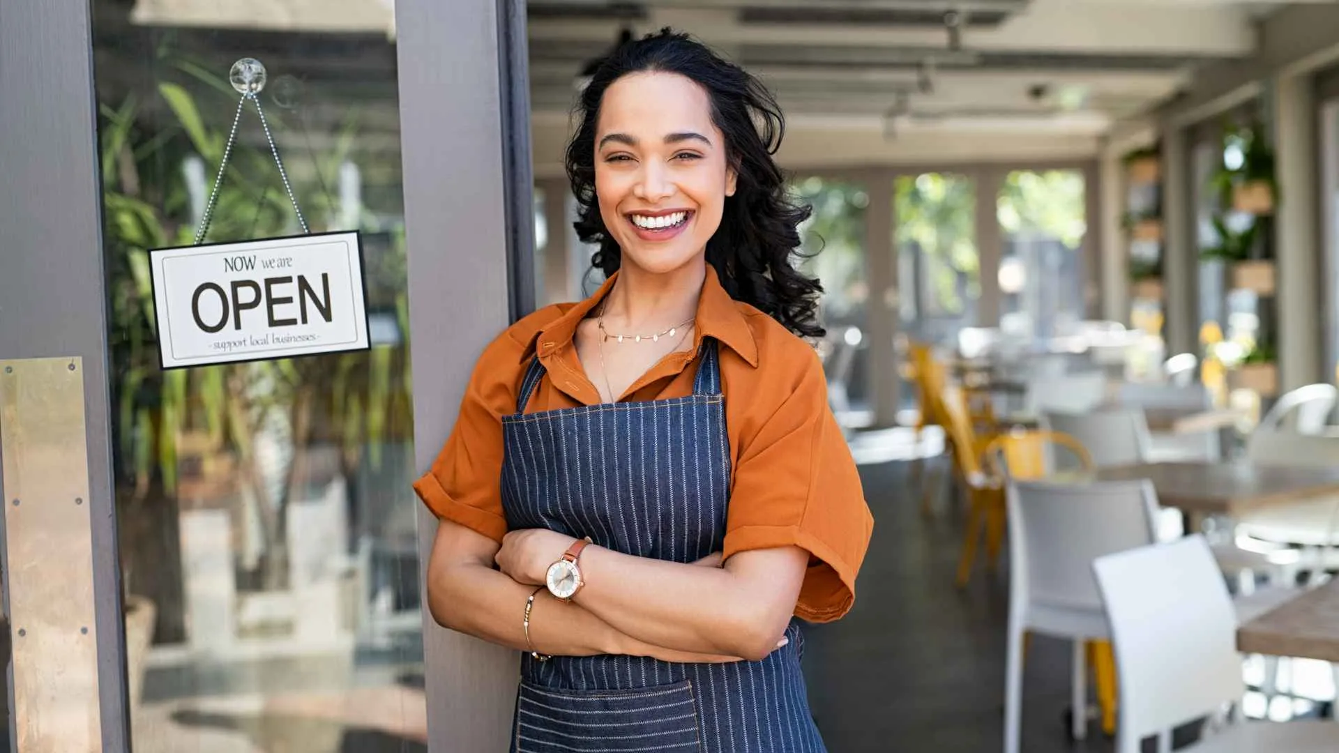 Portrait of happy waitress standing at restaurant entrance and looking at camera.