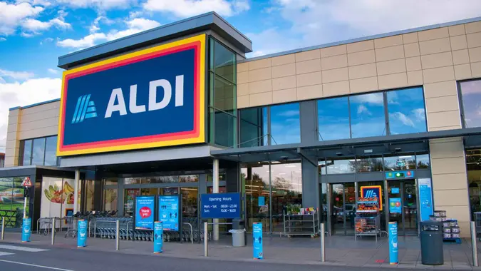 The frontage and brand logo of a branch of German discount retailer Aldi, taken in a local retail park on Wirral, UK on a sunny afternoon.