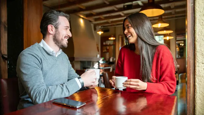 Happy Latin American couple drinking a cup of coffee at a cafe and smiling - food and drinks concepts.