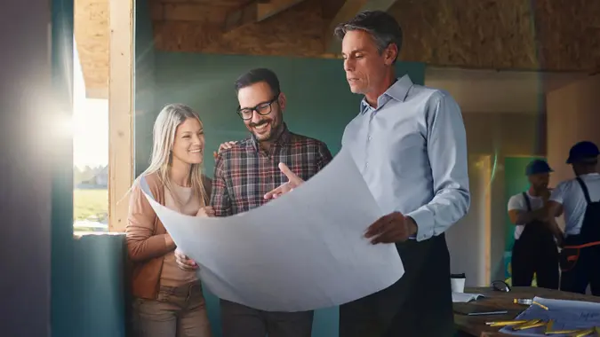 Happy couple analyzing blueprints with architect at construction site. stock photo