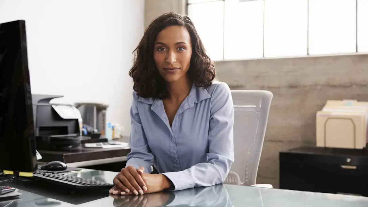 Young mixed race woman at office desk looking to camera.