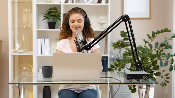 Woman vlogger looking at laptop and recording video with microphone close up.