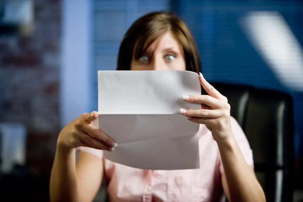 A woman looking at her mail (letter or bills)  in disbelief, shock! .