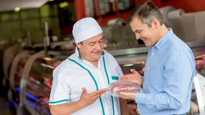 Happy man shopping at the butchery and talking to the man in charge.