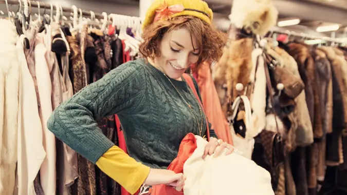 Happy young lady shopping in thrift store of vintage clothes stock photo