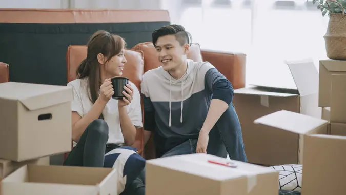 asia chinese couple sitting on floor resting after opening carton cardboard boxes in living room moving house.