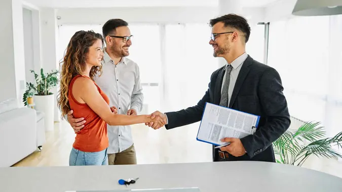Real estate agent with couple shaking hands closing a deal.