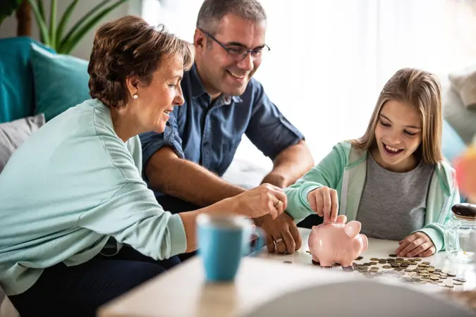 Three generation family is putting coins into piggy bank together.