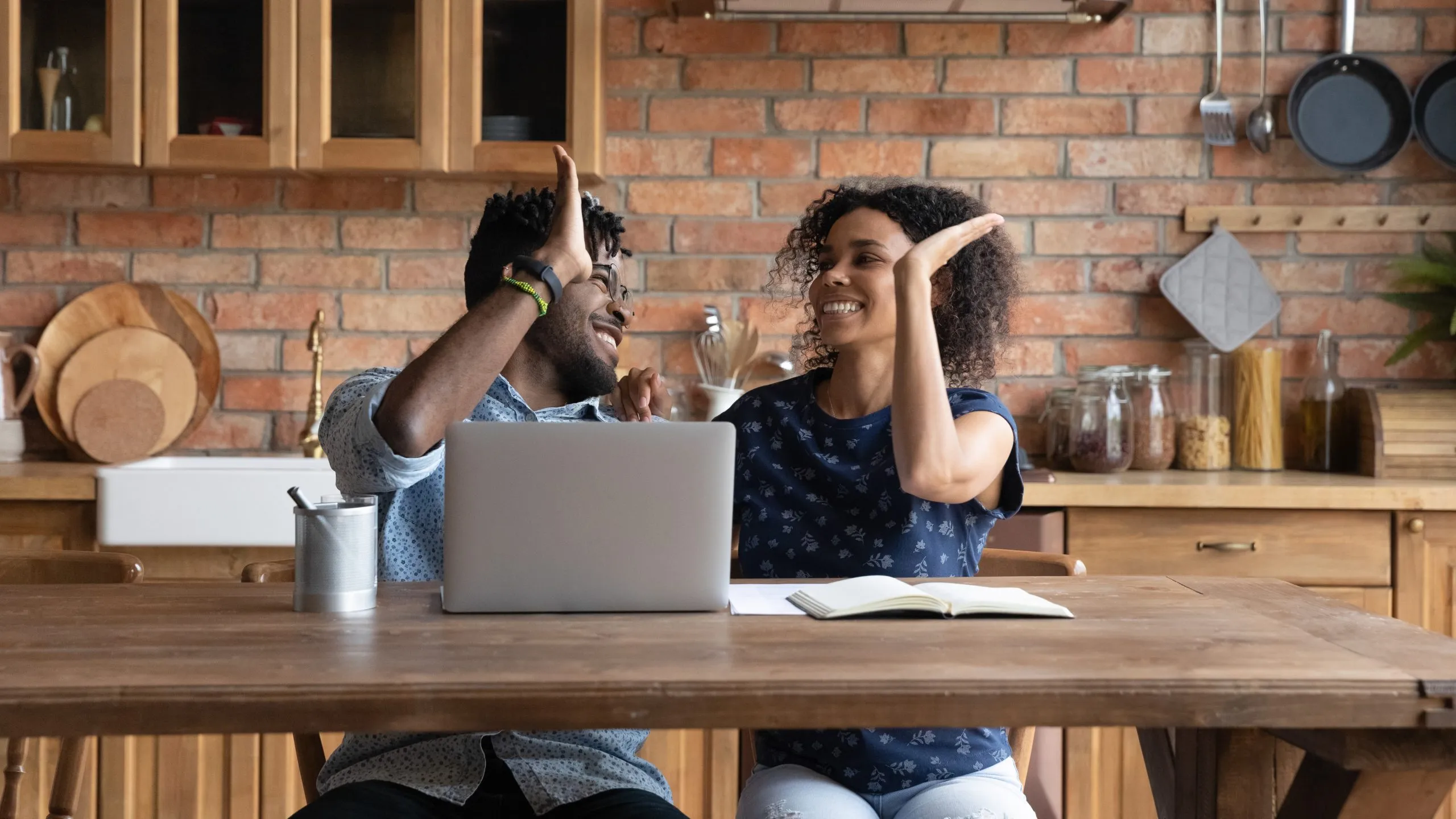 Happy successful Afro American couple celebrating financial achieve at laptop, giving high five.