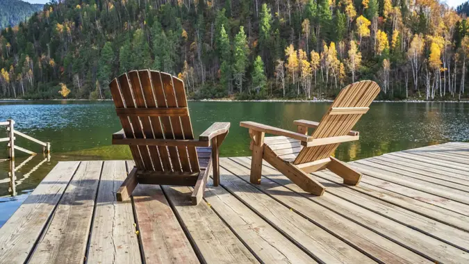 Two Adirondack chairs on a wooden dock overlooking a calm lake.