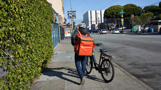 San Francisco, CA, USA - Feb 8, 2020: A DoorDash delivery worker walks his bike along the road in the Mission neighborhood of San Francisco, California.